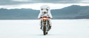 A person driving a motorcycle over a snow-covered field, eager to reach the elevated road.