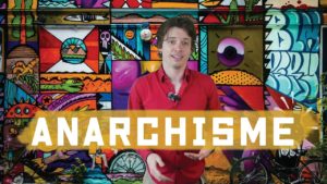 Someone in a red shirt is certainly standing in front of a wall of colorful graffiti, with the word "ANARCHISM" prominently displayed in the image.